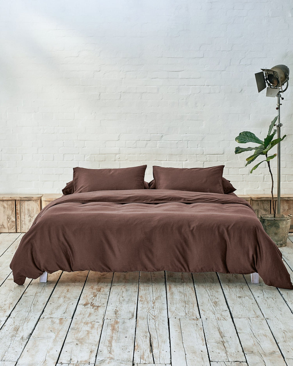 lifestyle shot of acorn brown bedding, situated in a modern bedroom with rustic wood flooring and white exposed brick walls