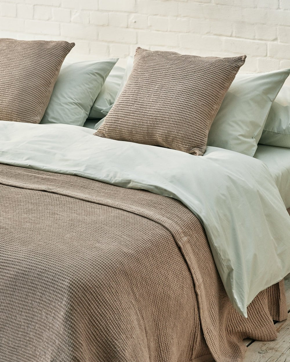 close up of beige scatter cushions and matching waffle throw on a sage green bed. 