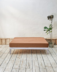 caramel brown fitted sheet in a modern bedroom with rustic wood floors and white walls.