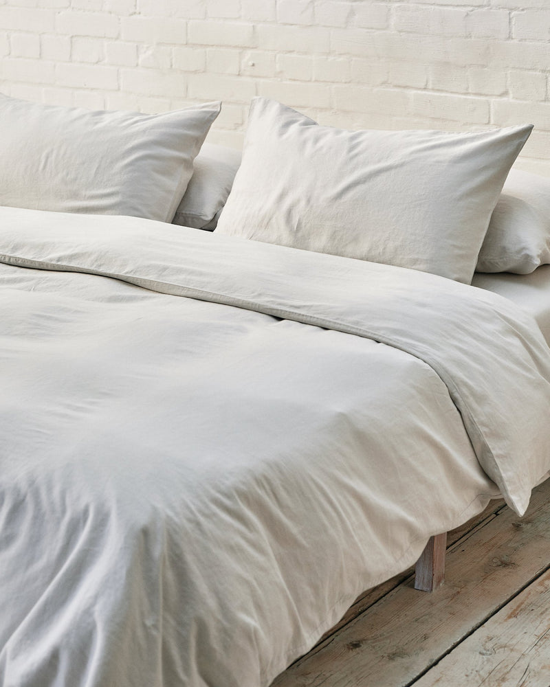 close-up shot of cloud grey bedding against white brick wall.