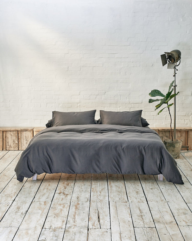 Modern bedroom with dark grey bedding and exposed brick wall