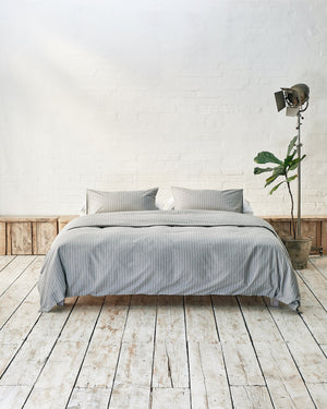 Modern bedroom with grey and white striped bedding and exposed brick wall